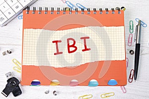 IBI word is written on a sheet in a cage lying on a notebook on the table next to stationery photo