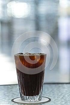 Ice Americano coffee in glass cup on glass table with outdoor background