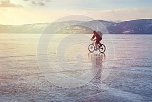 Ice biker traveler with backpacks on bike on ice of Lake Baikal. Against the background of sunset sky, ice surface. Winter sport