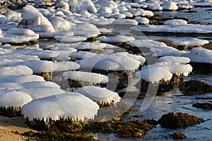 Ice caps on stones of the sea coast.  Winter landscape of coastal line. Icing on shore rocks in low winter temperature.