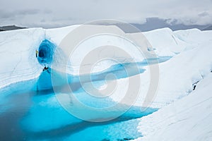 Ice cave above a large blue lake on top of the Matanuska Glacier in remote Alaska. Inside the cave an ice climber leads out of an