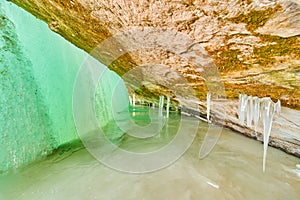 Ice cavern on frozen lake with entrance covered by frozen green waterfall