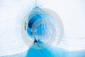 Ice cimber in front of an ice cave leading up from a canoe in a blue pool on the Matanuska Glacier