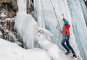 Ice climber dressed in warm winter climbing clothes, safety harness and helmet climbing frozen waterfall using two Ice climbing