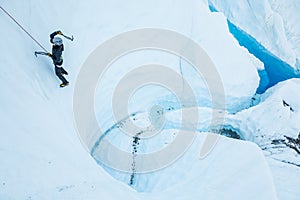 Ice climber over complex canyon and blue pool on the Matanuska Glacier in Alaska