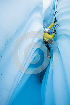 Ice climber pressing his back across narrow canyon of ice on the Matanuska Glacier in Alaska