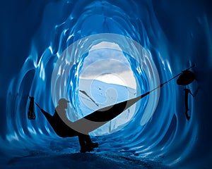 Ice climber resting in hammock inside a deep blue ice cave in the Matanuska Glacier of Alaska