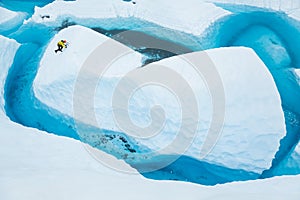 Ice climber soloing up an island of ice that looks like an iceberg in a large blue pool on the Matanuska Glacier