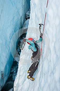 Ice climber swinging ice tool inside a deep crevasse on a glacier in Alaska