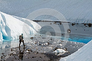 Ice climber trekking across flat valley to a blue pool on the Matanuska Glacier in Alaska