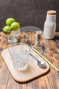 Ice for a cocktail and limes in glass on a wooden table