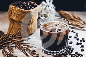 Ice coffee black in a glass and coffee beans. Cold summer drink on wooden table with copy space.