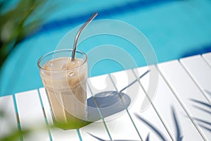 Ice coffee Cyprus Frappe Fredo against blue clear water of the swimming pool, on white table, with metal straw . Summer photo