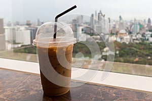 Ice coffee in plastic glass on the table with park and city in background, relax before starting hardwork in a day