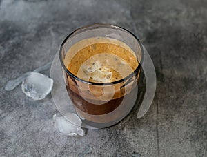 Ice coffee in a tall glass, ice cubes on a gray wooden table. Cold summer drink with tubes on a black background with