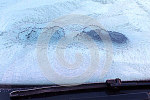 Ice-covered frozen car windshield with snow patterns