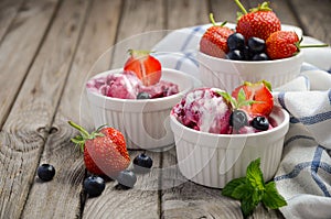 Ice cream with blueberries and strawberries in white bowl on rustic wooden background