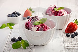 Ice cream with blueberries and strawberries in white bowl on white wooden background