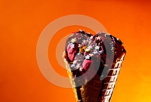 Ice cream with chocolate topping in waffle cone at orange background