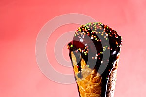 Ice cream with chocolate topping in waffle cone at pink background