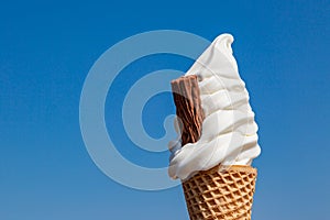 An ice cream cone against a clear blue sky, with space for text