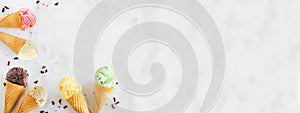 Ice cream cone border with a variety of flavors, top view over a white marble banner background