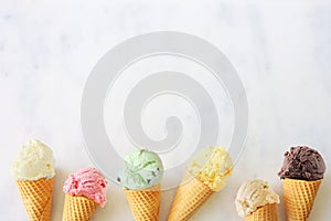 Ice cream cone bottom border with a variety of flavors overhead on a white marble background