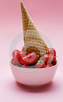 Ice cream cone on fresh strawberries in a bowl on pink background