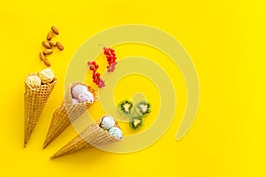 Ice cream in cone with kiwi, hazelnut and wineberry on yellow backgroung top view copyspace