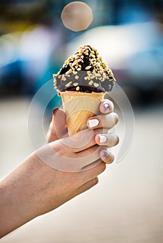 Ice cream cone with nuts and chocolate in hands