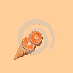Ice cream cone with sliced tangerine on peachy background. Flat lay. Minimal summer concept