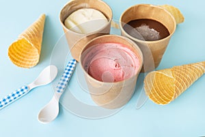 Ice cream in a craft box with different flavors - strawberry, chocolate, vanilla stands on a blue background along with a waffle