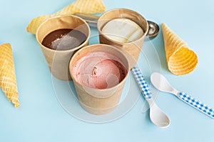 Ice cream in a craft box with different flavors - strawberry, chocolate, vanilla stands on a blue background along with a waffle