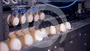 Ice-cream cups are being grabbed and relocated by metal tongs from a rotating conveyor to a linear one