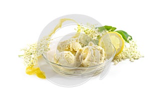 Ice cream from elderberry flowers in a glass bowl, lemon peel and slices and some fresh blossoms isolated on a white background,