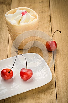 Ice cream in a glass with cherry in a white plate/ice cream in a glass with cherry in a white plate on a wooden background.