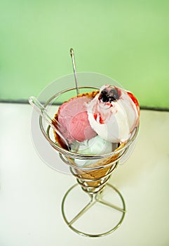 Ice Cream Holders. Strawberry, mint, vanilla with sour cherry ice cream in large waffle cone in holder, spoon.