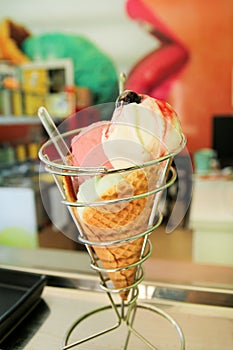 Ice Cream Holders. Strawberry, mint, vanilla with sour cherry ice cream in large waffle cone in holder, spoon.