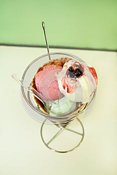 Ice Cream Holders. Strawberry, mint, vanilla with sour cherry ice cream in large waffle cone in holder, spoon.