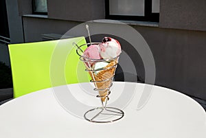 Ice cream holders on table. Strawberry, mint, vanilla with sour cherry ice cream in large waffle cone in holder.