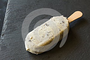 Ice cream lolly with white chocolate coating and dark chocolate cookie crumbs isolated on black background - side view