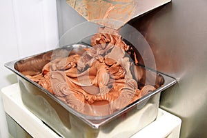 Ice cream making machine produces black chocolate ice cream flavors and it falls into steel container.