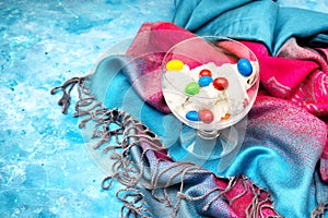 Ice cream with multicolor candies in a glass bowl standing on a colorful cloth and light blue background. Bright summer dessert