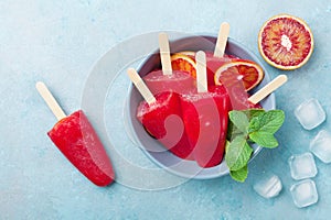 Ice cream or popsicles decorated mint leaves and orange slices on blue table top view. Frozen fruit juice. Summer food.