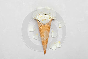 Ice cream of rose flowers in waffle cone on light gray background from above, beautiful floral decoration, vintage color, flat lay