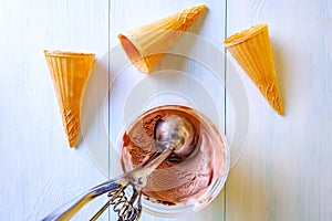 Ice cream set - waffle cones, chocolate ice cream, a spoon for making balls on a light wooden background.