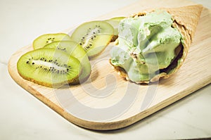 ice cream in a wafer cup and kiwi slices/ice cream and kiwi slices on a wooden tray and marble background, selective focus