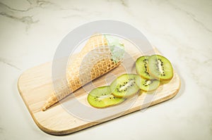 Ice cream in a wafer cup and kiwi slices/ice cream and kiwi slices on a wooden tray and marble background, top view