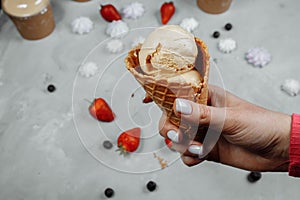 Ice cream in a waffle cone on a light background in a hand. The ice cream is melting. Waffle cones and strawberries in