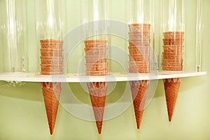 Ice cream waffle cones on dispenser. Ice cream cornets packed in dispenser on the wall of the store. Italian pastry shop.